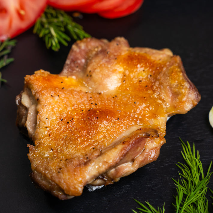 Roasted Joyce Farms Poulet Rouge® Heritage Boneless, Skin-On Whole Chicken Legs on a black background with tomatoes and dill.