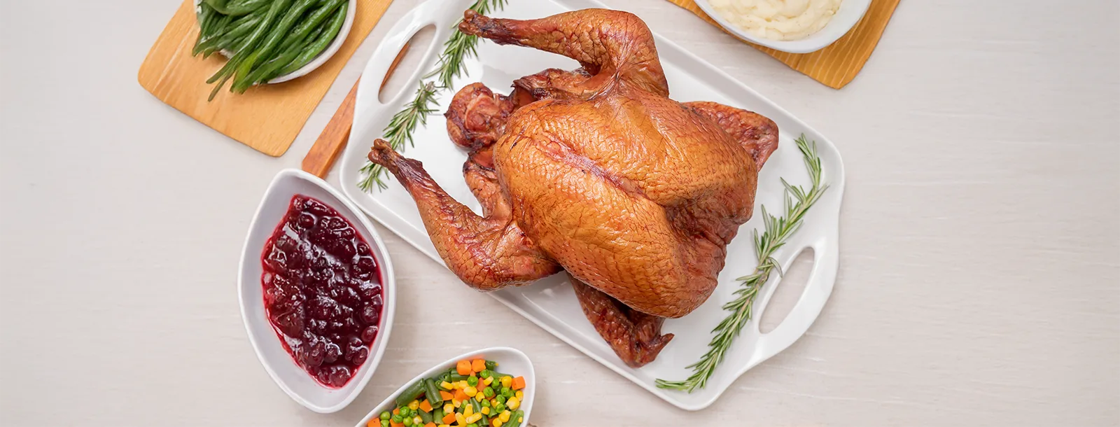 A beautifully roasted Joyce Farms Heritage Black Turkey displayed on a white serving platter, garnished with fresh sprigs of rosemary.