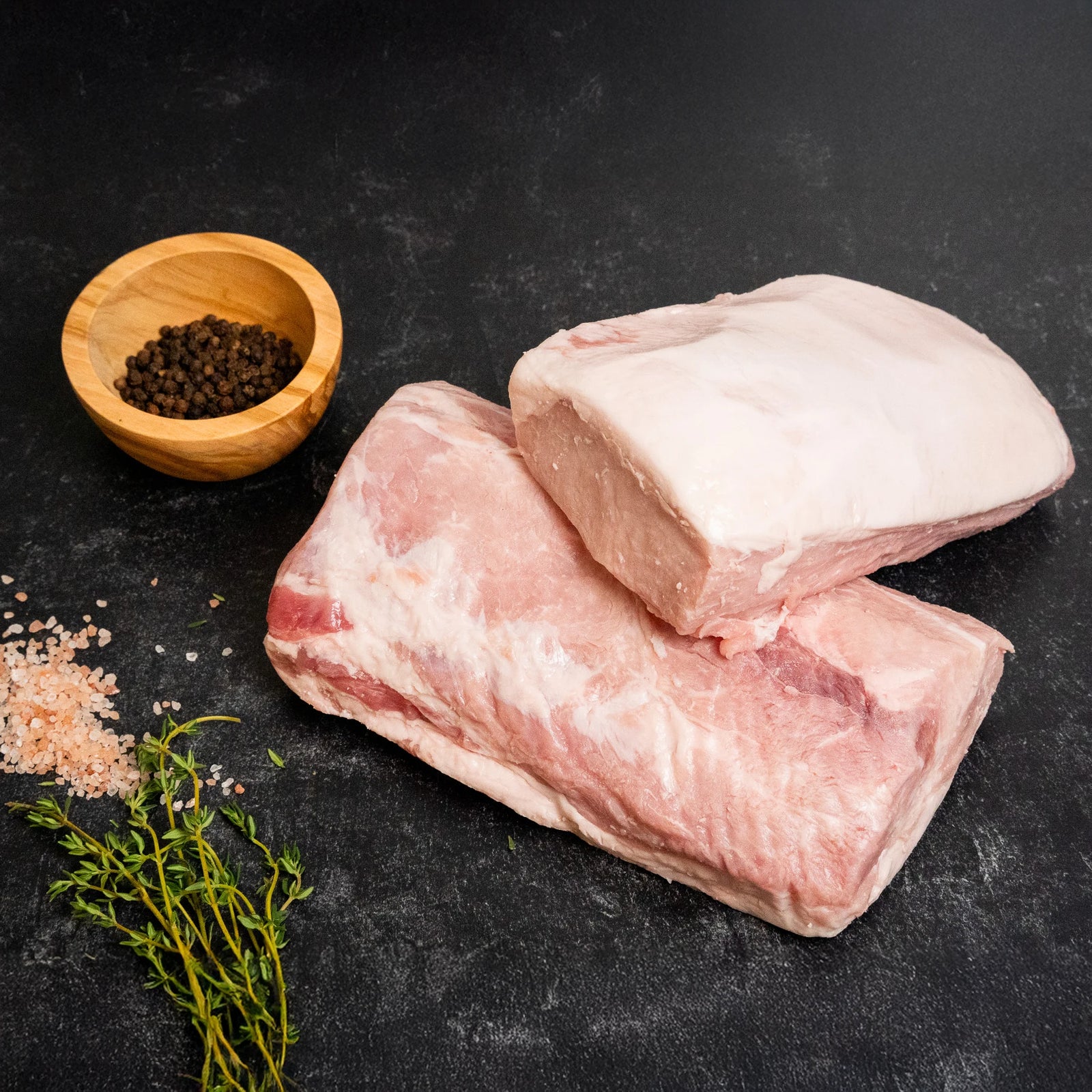 Raw pork sirloin end loin portions on a dark surface with sea salt, black pepper, and fresh thyme.