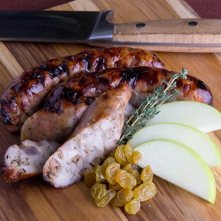Apple Raisin Naked Chicken Sausages, sliced on a cutting board with apples, raisins, and thyme.