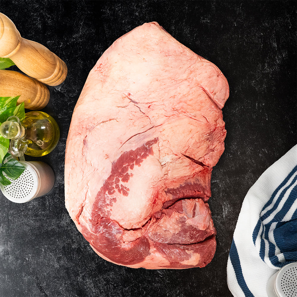 Raw piece of Joyce Farms Signature Heritage Brisket meat on a dark surface with seasonings and a towel