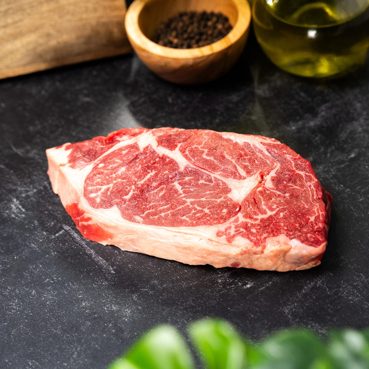 Raw steak on a dark surface with peppercorns and olive oil in the background
