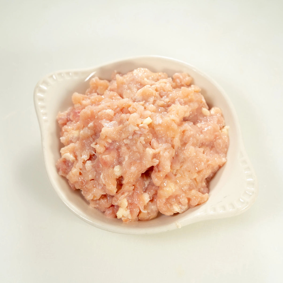 raw joyce farms naked ground chicken in a white bowl with a light background