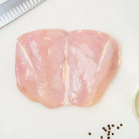 Raw Joyce Farms Boneless, Skinless Naked Chicken breast on a cutting board with a knife and peppercorns.