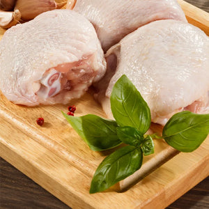 Raw Antibiotic-Free Bone-In, Skin-On Naked Chicken Thighs on a wooden board with basil leaves.