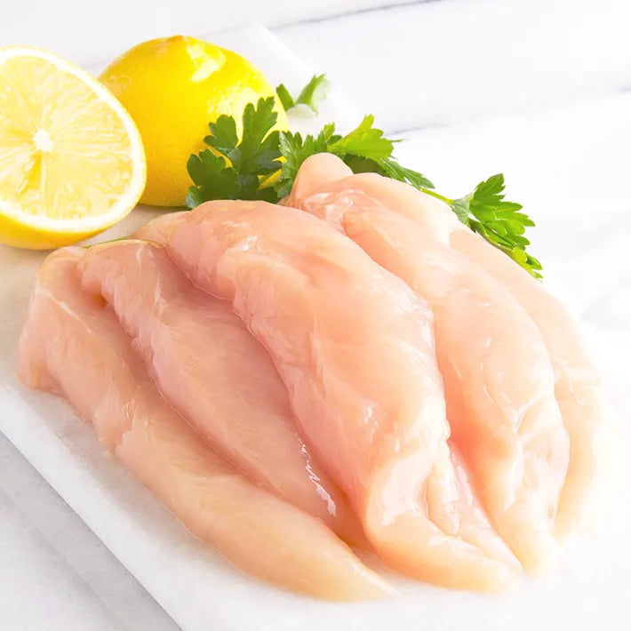 Raw Antibiotic-Free Naked Chicken Tenders on a white surface with lemon and parsley.