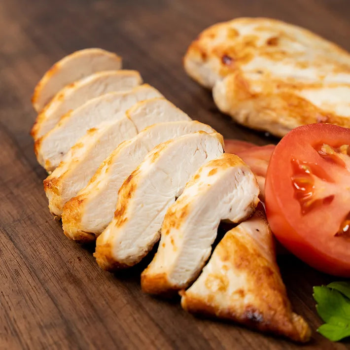 Sliced, cooked Poulet Rouge® Boneless Skinless Chicken Breast from Joyce Farms, a heritage breed known for its slow-growing, pasture-raised, and air-chilled process, displayed on a wooden cutting board with a tomato garnish. Rich in flavor.