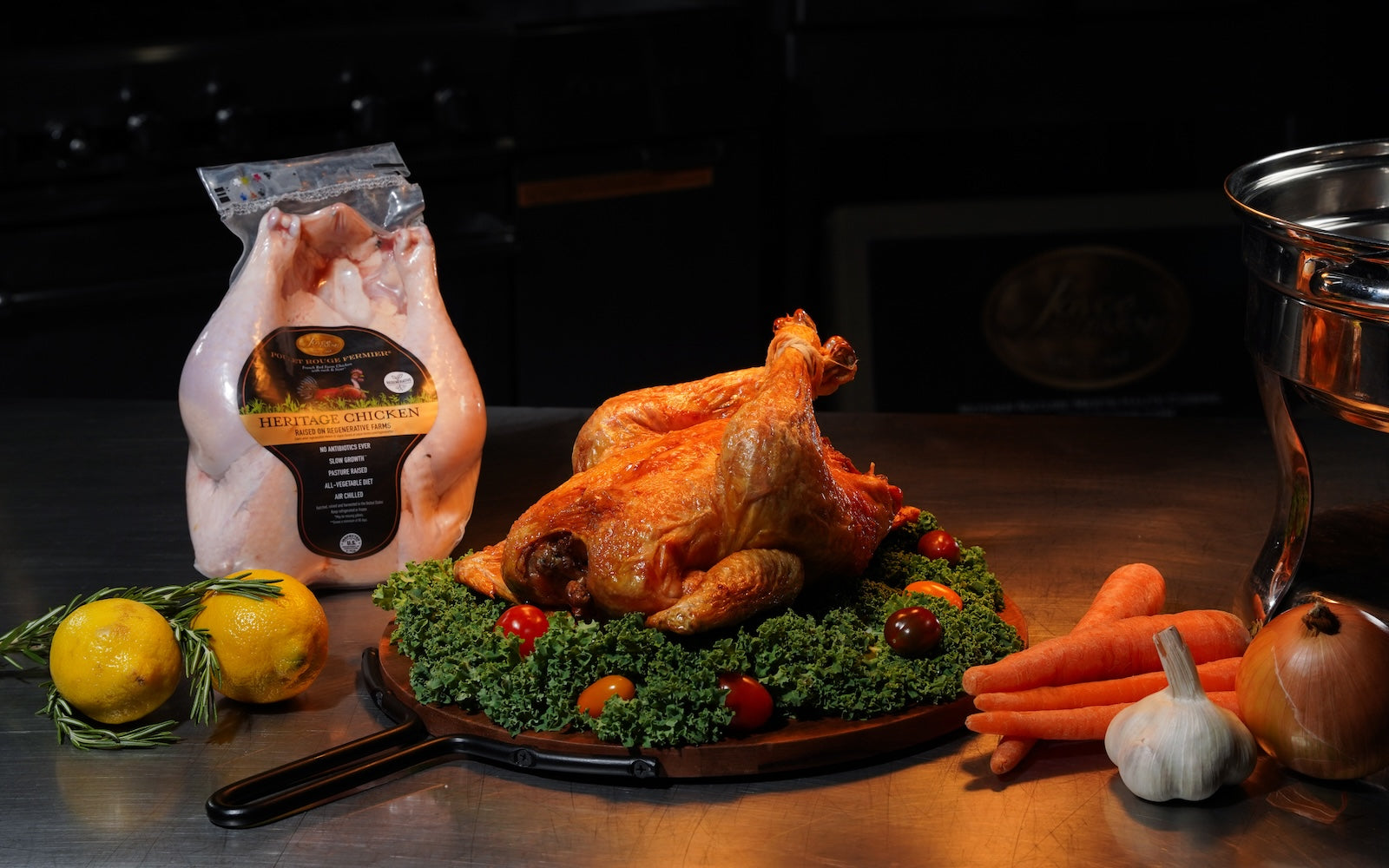 Image of cooked Poulet Rouge® Heritage Chicken from Joyce Farms on bed of greens and baby tomatoes, with packaged, raw Poulet Rouge® Heritage Chicken in the background