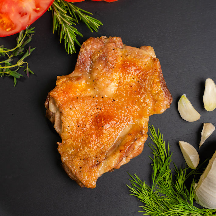 A piece of Poulet Rouge® Heritage boneless chicken on a black surface with tomatoes and garlic from Joyce Farms.