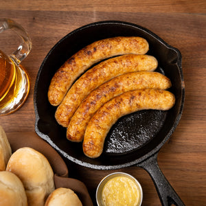 4 Cooked Joyce Farms Naked Chicken Bratwurst links in a cast iron pan 