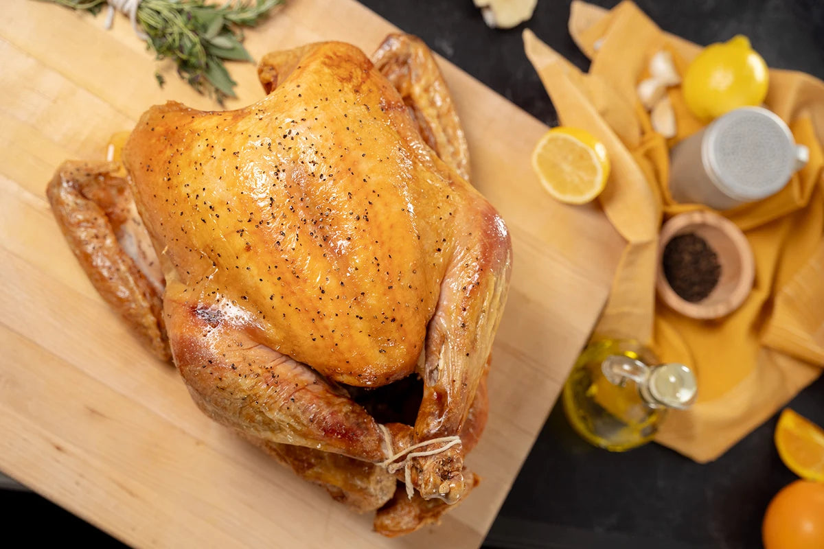 Roasted turkey on a wooden cutting board with herbs and lemons in the background