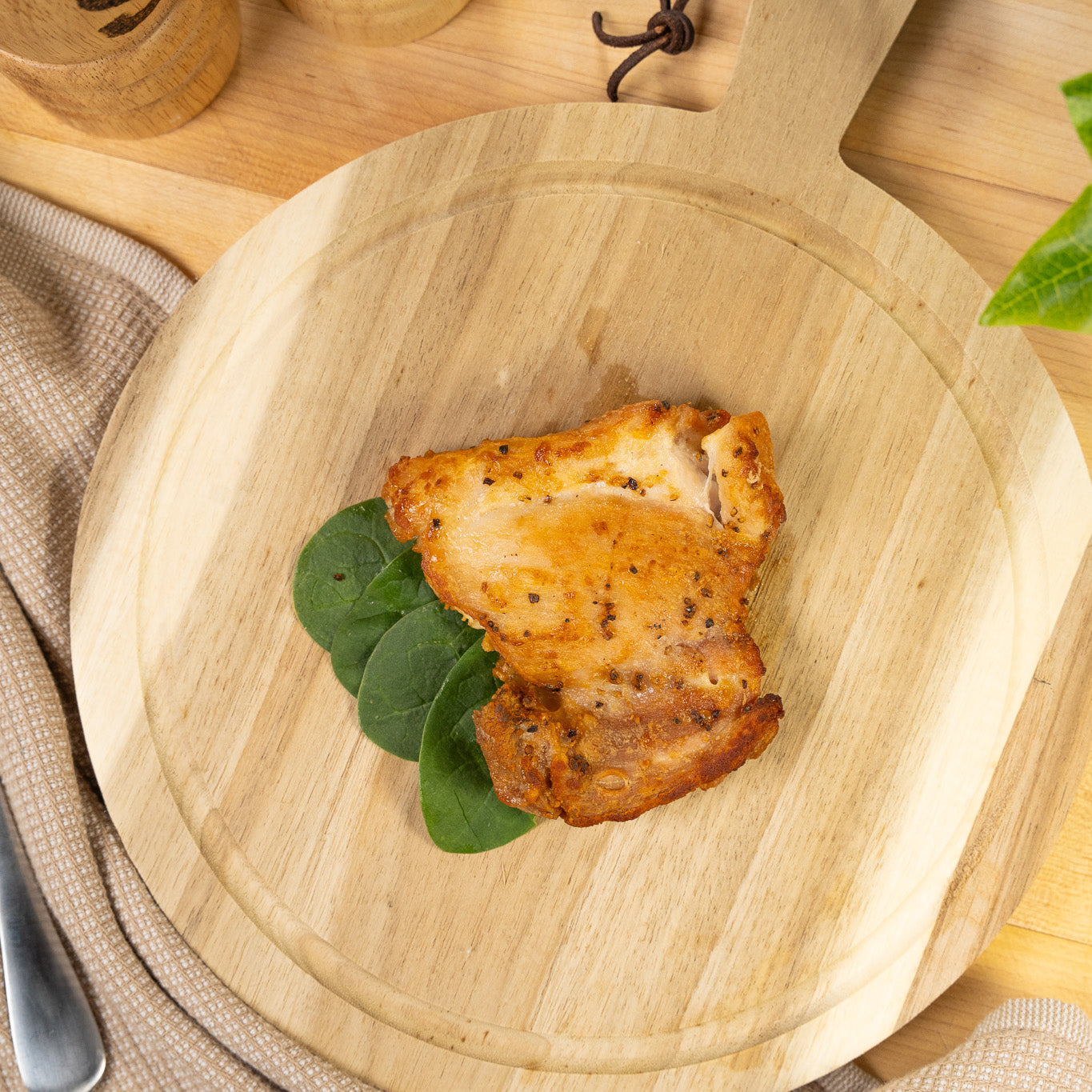 Grilled boneless skinless joyce farms chicken thigh on a wooden cutting board with a leafy green garnish.