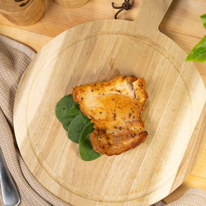 Grilled boneless skinless joyce farms chicken thigh on a wooden cutting board with a leafy green garnish.