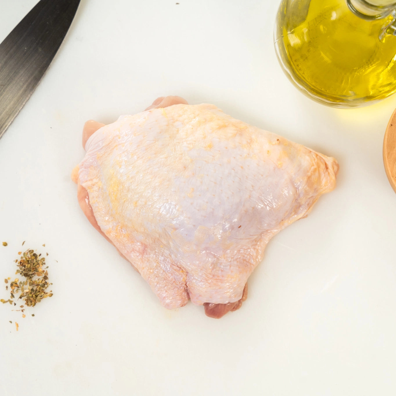 Raw chicken thigh on a cutting board with olive oil and herbs