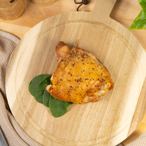 Cooked Bone-In, Skin-On Joyce Farms Naked Chicken thigh resting on a small wooden cutting board with spinach on the side