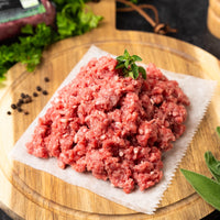 Joyce Farms Heritage Aberdeen Angus ground beef meat on parchment paper on top of a wooden cutting board with herbs and spices.