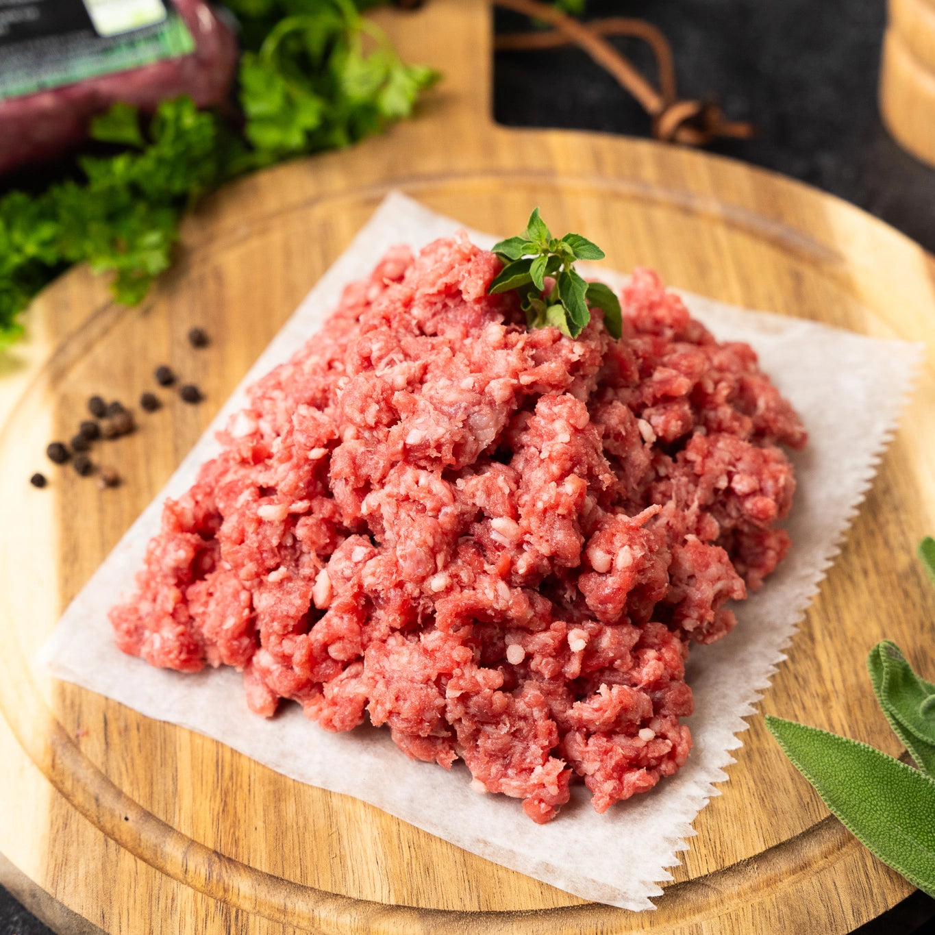 Joyce Farms Heritage Aberdeen Angus ground beef meat on parchment paper on top of a wooden cutting board with herbs and spices.