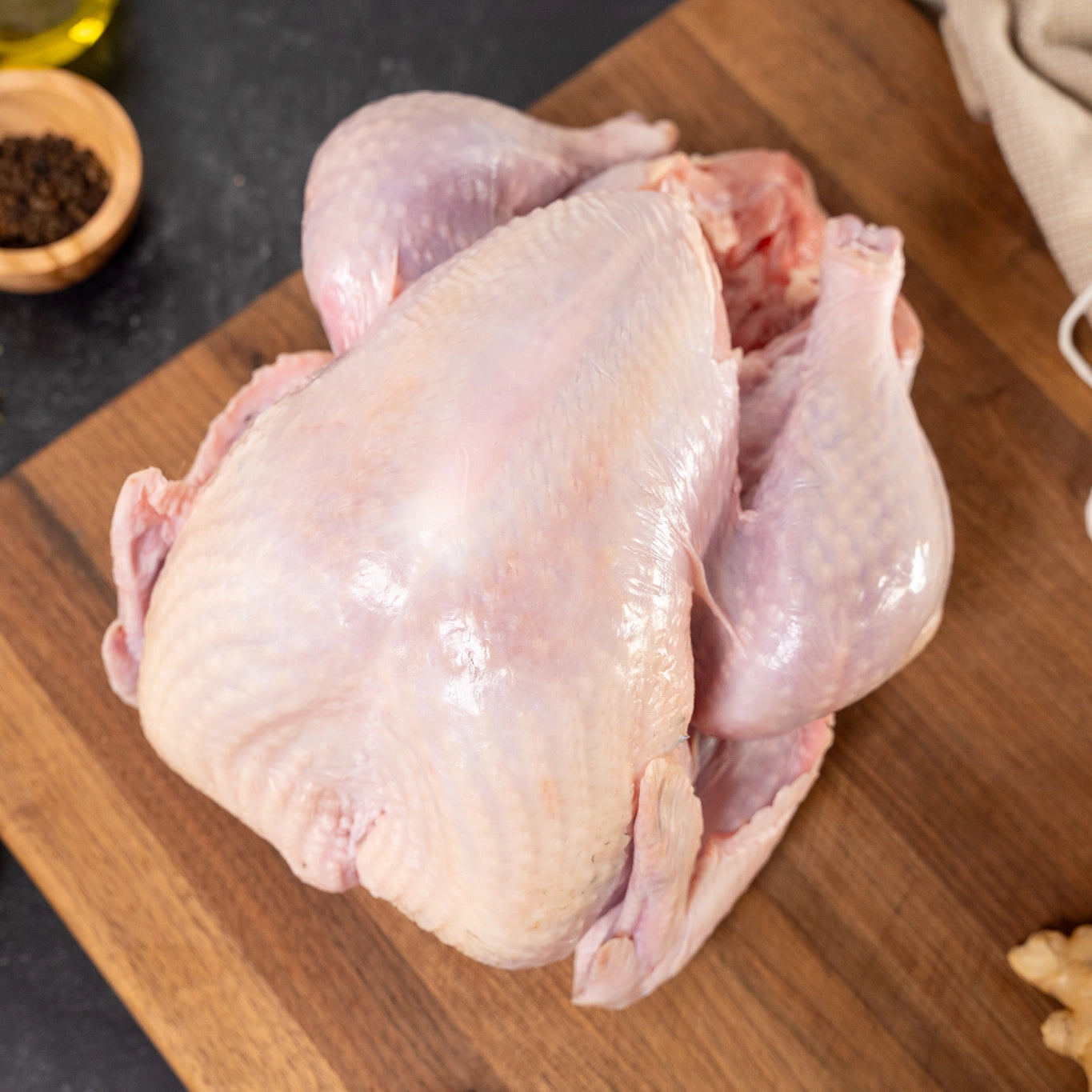 Resting on a wooden cutting board on the counter, is a raw Heritage Black Turkey bird illustrating it's color, thin skin, and unique body conformation. 