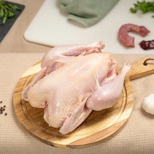 A Joyce Farms Heritage Poulet Rouge® raw whole bird rests on circular wooden cutting board. A raw neck and liver sit on a cutting board in the background.