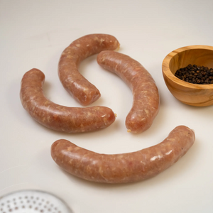 4 raw, unpackaged Naked Chicken Bratwurst links from Joyce Farms shown on a cutting board