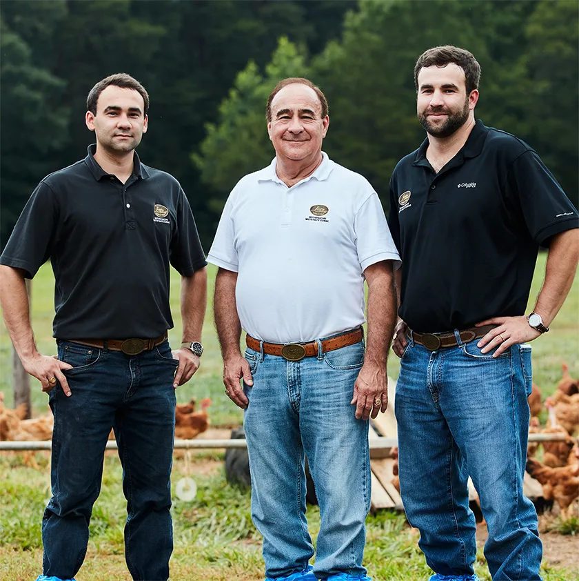 Three generations of the Joyce family standing proudly on the farm where their Poulet Rouge® Heritage Chickens are raised on pasture, which can be seen in the background. From left to right: Stuart Joyce, Ron Joyce, and Ryan Joyce.
