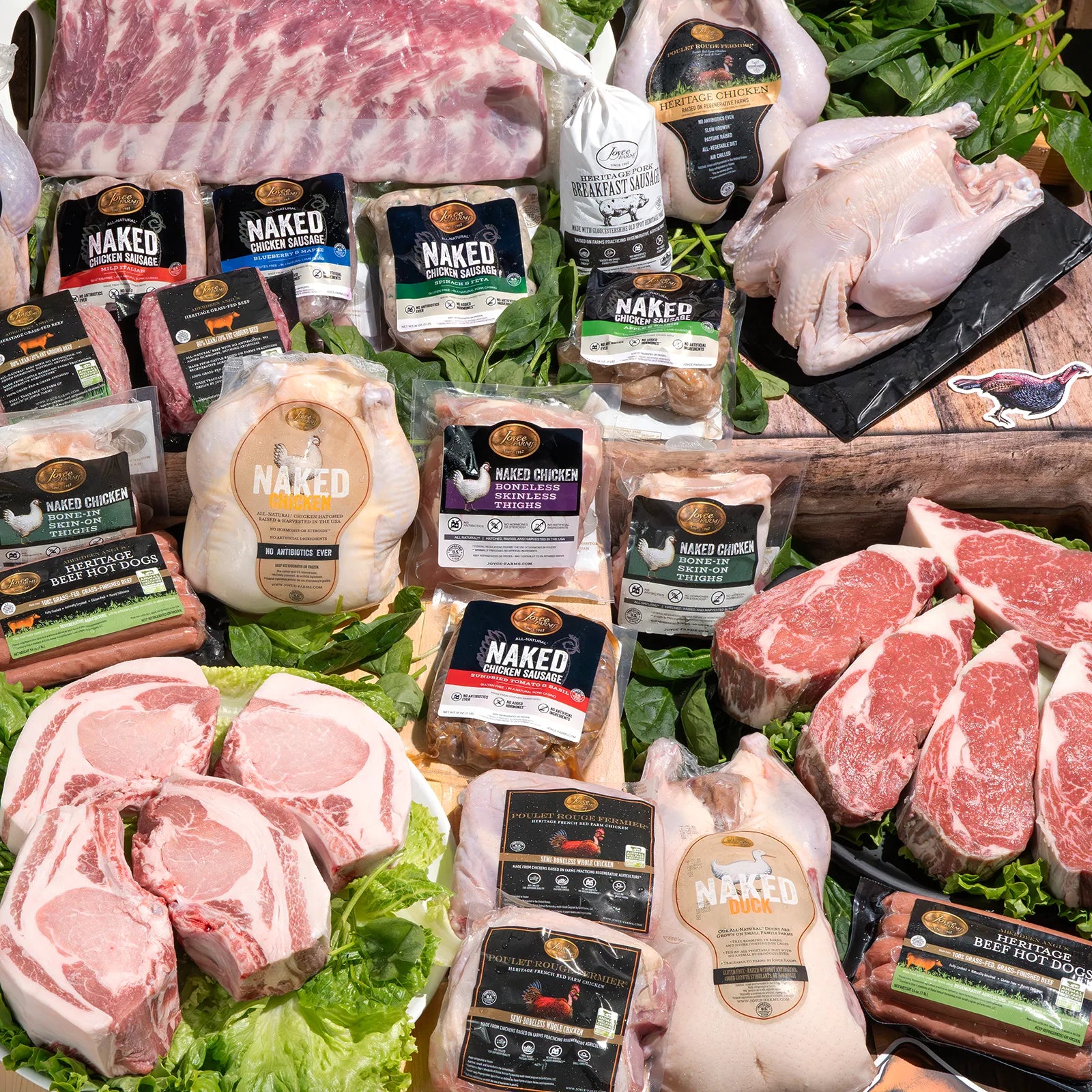 A colorful assortment of Joyce Farms' premium meat products displayed on a rustic wooden surface. The variety includes whole chickens, beef cuts, sausages, and packaged poultry, showcasing the diversity and quality of their offerings. The vibrant packaging and fresh appearance highlight the brand's commitment to high-quality, flavorful meats.