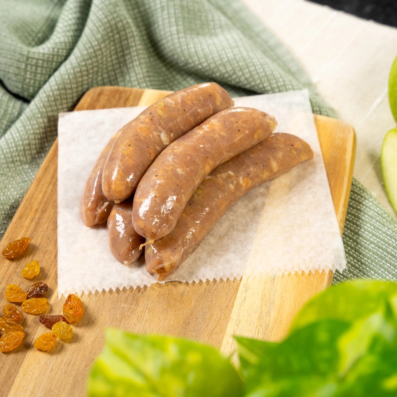 Apple Raisin Naked Chicken Sausages, raw on a cutting board with fresh apples, and raisins