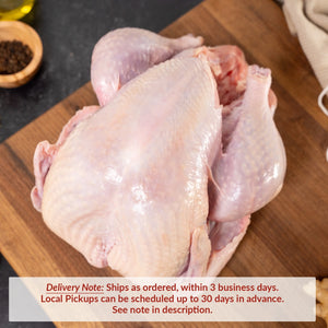 A whole raw turkey resting on a wooden cutting board, with peppercorns, garlic, herbs, and a bottle of oil nearby on a dark kitchen surface. Text overlay reads: “Delivery Note: Ships as ordered, within 3 business days. Local Pickups can be scheduled up to 30 days in advance. See note in description.