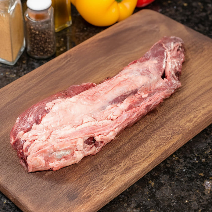 Raw Joyce Farms Signature Angus Heritage Beef Tenderloin on a wooden cutting board with spices and peppers in the background