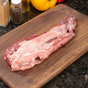 Raw Joyce Farms Signature Angus Heritage Beef Tenderloin on a wooden cutting board with spices and peppers in the background