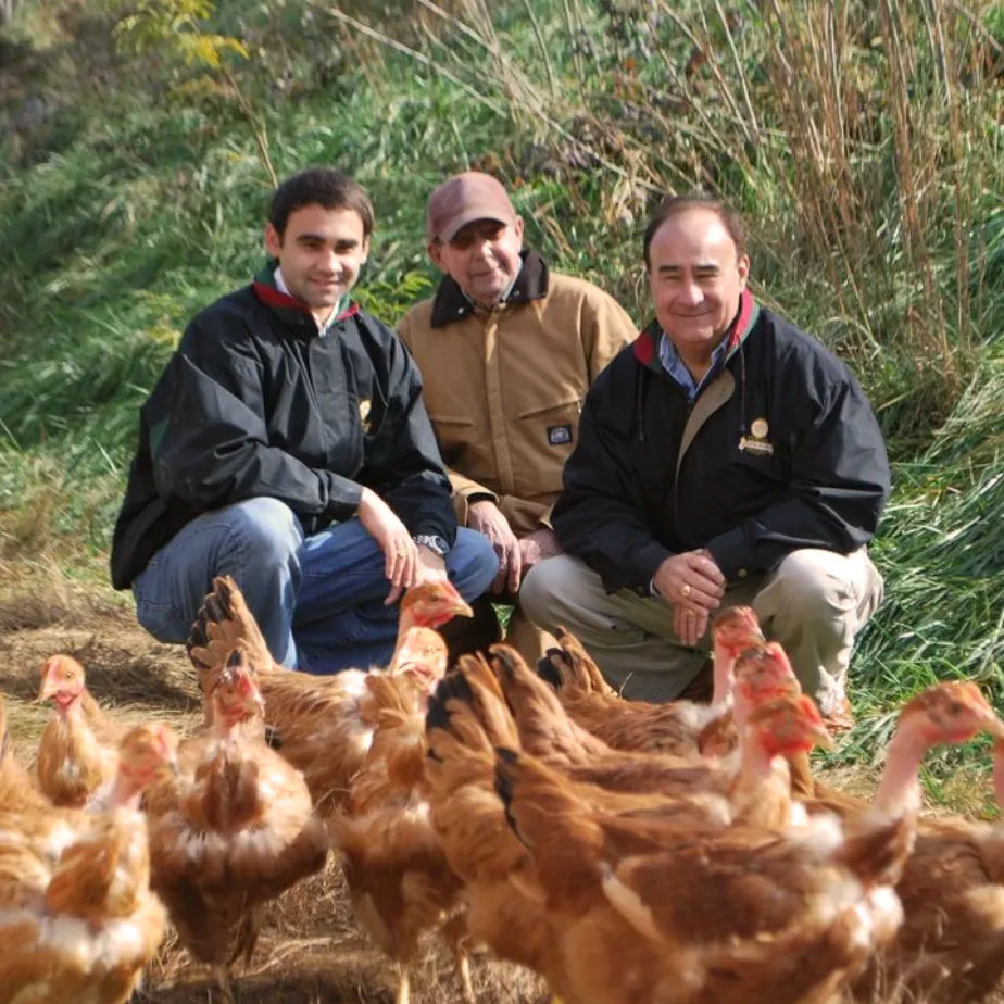 Stuart Joyce, Charlie Coble, and Ron Joyce standing together on a farm, proudly showcasing a Poulet Rouge® Heritage Chicken. 