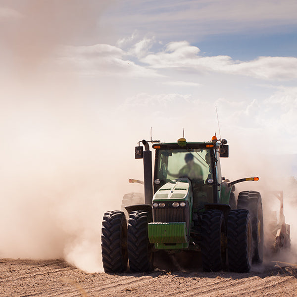 A tractor tilling dry, dusty soil under a partly cloudy sky, illustrating the challenges of conventional farming practices.