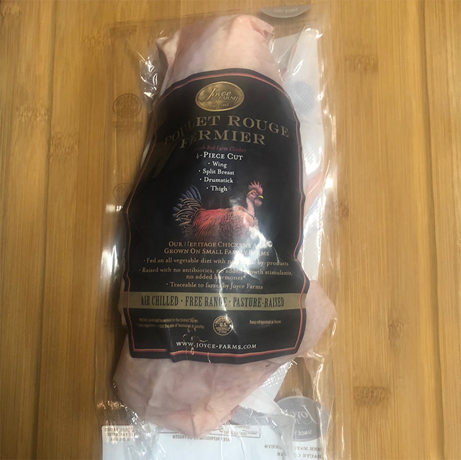 A Poulet Rouge® 4-Piece Cut, Half Heritage Chicken (2 packs) in a plastic bag on a wooden table by Joyce Farms.